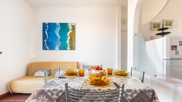 Een eetgedeelte met een tafel voor vier personen, een bank en een schilderij van een golf aan de muur.