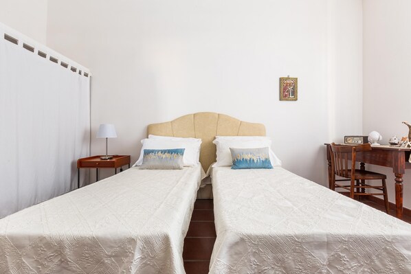 A room with two single beds, a wooden desk with a chair, a lamp, and a picture on the wall.