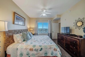 A hotel room with a bed, a dresser, a ceiling fan, a TV, and a window with curtains.