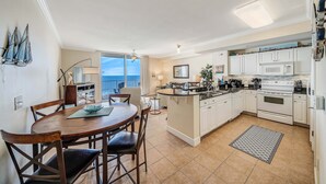 A modern kitchen with white cabinets, a central island, and a dining area with a round table and chairs.