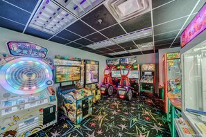 Une salle d’arcade proposant divers jeux, un présentoir pour les prix et un sol décoré de motifs en forme d’étoiles.