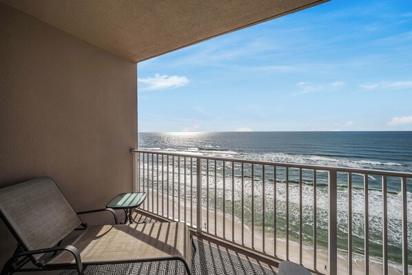 A balcony with a view of the ocean, a chair, and a small table.