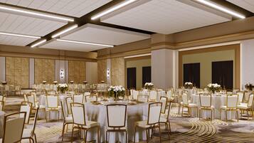 A spacious banquet hall with round tables, white chairs, and floral centerpieces.