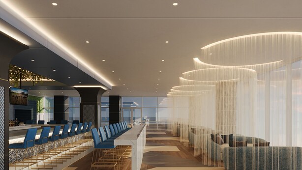 A modern hotel lobby with a long reception desk, blue seating area, and a staircase leading to upper floors.