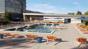 A pool area with multiple lounge chairs and umbrellas, a pool, and a modern building in the background.