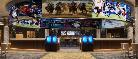 A lobby with multiple screens displaying sports events, a reception desk, and a patterned carpet.