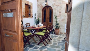 An open wooden door leading to a stone-floored courtyard with a table and chairs, a potted plant, and a stone wall.