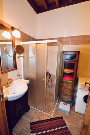 Un baño con lavamanos, espejo, ducha y un perchero con toallas de colores.