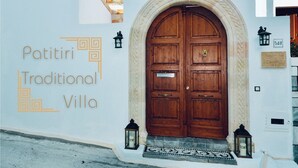 A traditional villa with a large wooden door, a white wall with the text "Patitiri Traditional Villa", and two lanterns on either side of the door.
