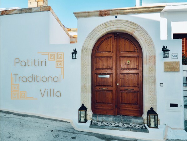 Una villa tradicional con una puerta de madera grande, una pared blanca con el texto 