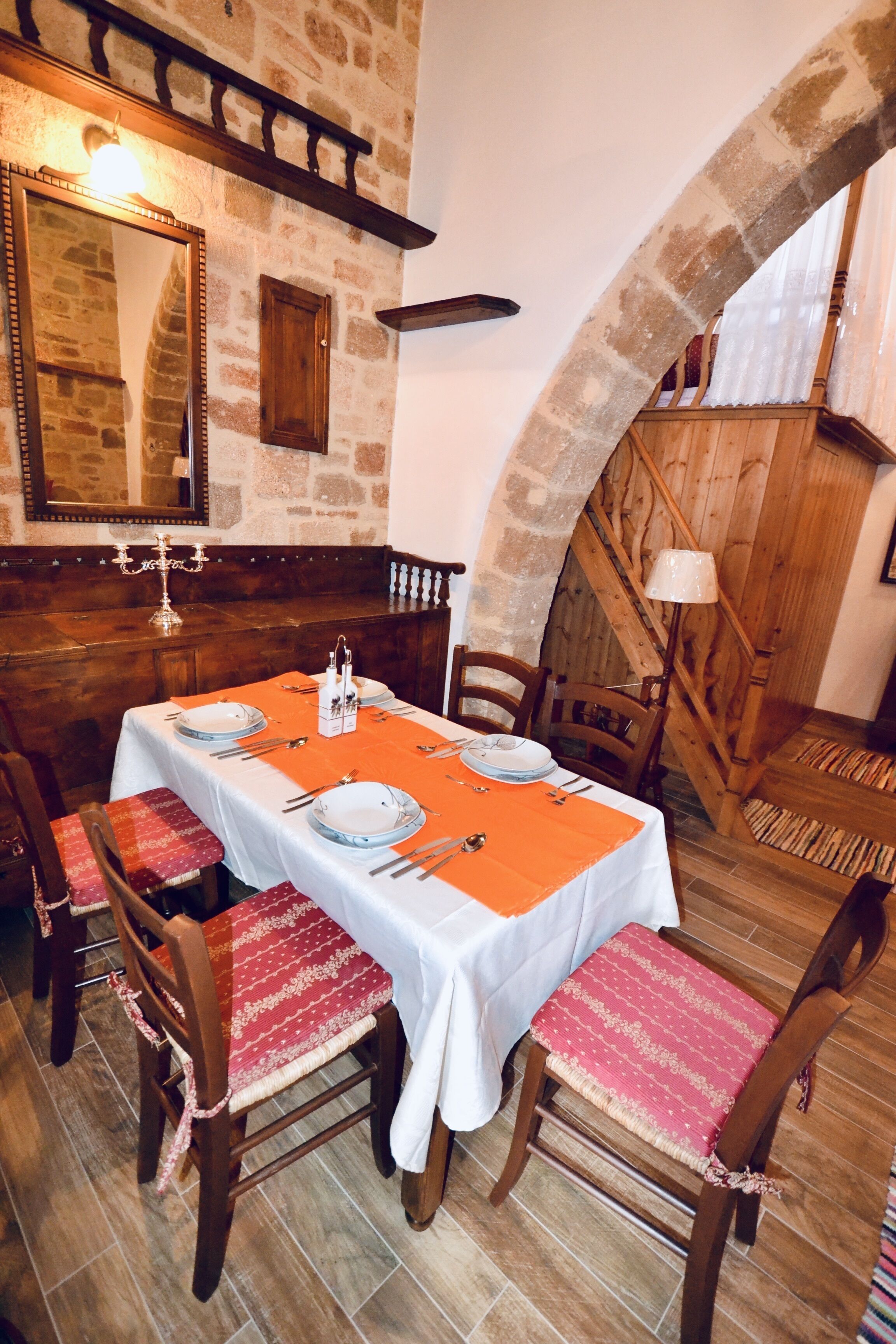 A dining area with a stone wall, wooden staircase, and a table set for four with chairs.