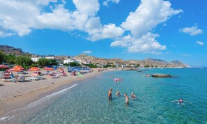 A beach with clear water, umbrellas, and people swimming.