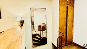 Une pièce avec un puits de lumière, un bureau en bois, un miroir, une porte et une chaise.