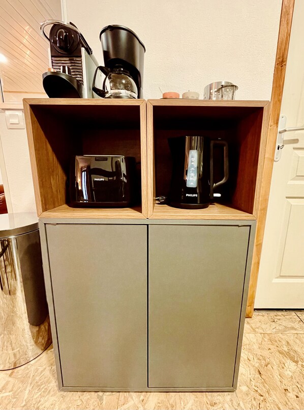 A compact kitchenette with two coffee makers and a small trash bin.