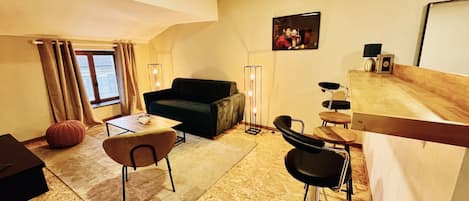A modern living room with a sofa, a coffee table, a dining table with chairs, and a bar area.