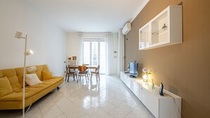 A modern living room with a yellow sofa, a dining table, and a TV on a white cabinet.
