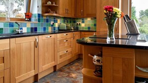 A kitchen with wooden cabinets, a tiled backsplash, and a window with a view of trees. - 2 Bedroom bungalow Aberdeen within the beautiful countryside. (Aberdeen)