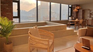 A modern living room with a large window, a built-in bench, wicker furniture, and a dining area. - Poolvilla Gaon (Busan)