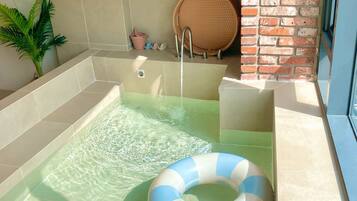 Un área de spa con un jacuzzi, dos anillos hinchables, una planta en maceta y una pared de ladrillo.