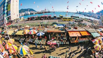 A bustling market area with various stalls and umbrellas, a bridge in the background, and a body of water.
