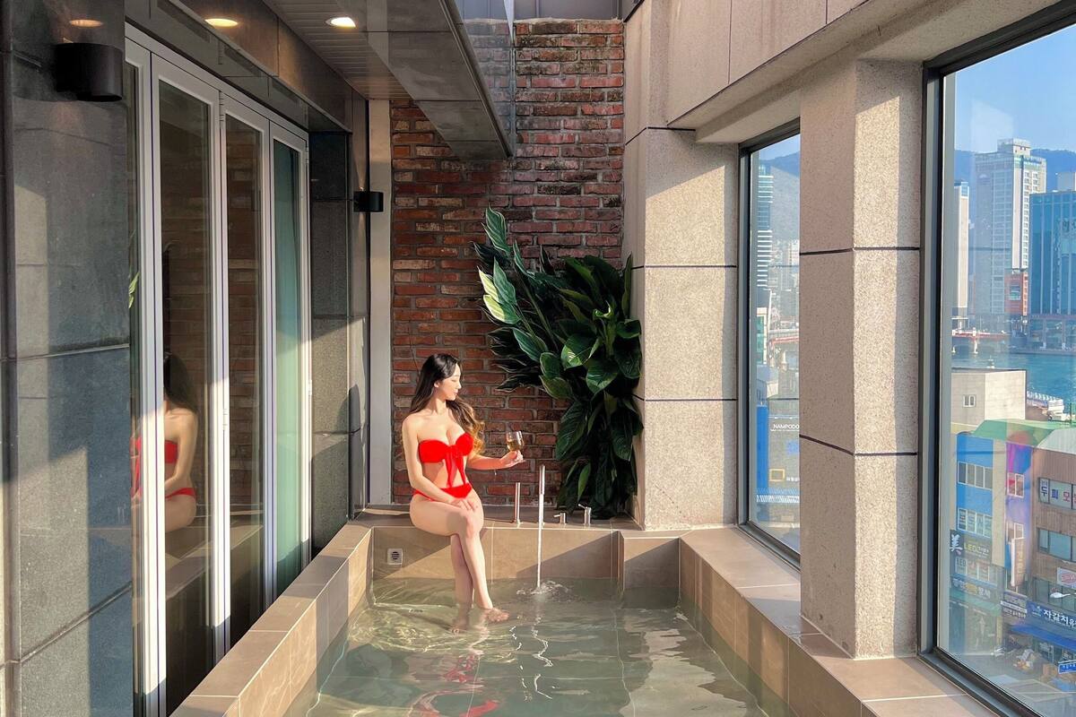 A modern indoor pool with clear glass walls, a brick wall, and a large window offering a city view.