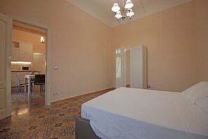 A bedroom with a bed, a wardrobe, and a small kitchenette in the background.