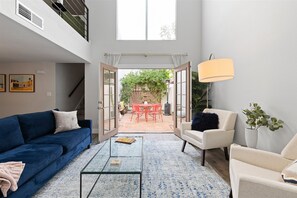 Relax in this spacious living room with a mezzanine level, sofa, armchair, and floor lamp, opening to a patio with a table and chairs.