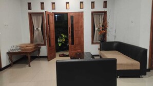 A living room with a black sofa, a wooden coffee table, and a door leading to another room. - Villa Ricky Gunung Bromo  (Ngadisari)