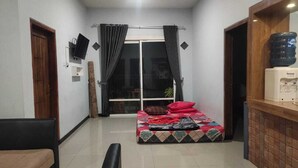 A compact living space with a bed, a TV mounted on the wall, a water dispenser, and a sliding glass door leading to a balcony. - Villa Ricky Gunung Bromo  (Ngadisari)