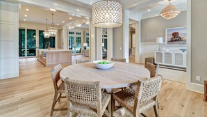A spacious dining area with a round table and wicker chairs, a large pendant light, and a view of the kitchen and dining room through glass doors. - Ultra Luxe Home, Pool & Spa, Screened Porch, 5 Min Walk to Beach (Hilton Head Island)