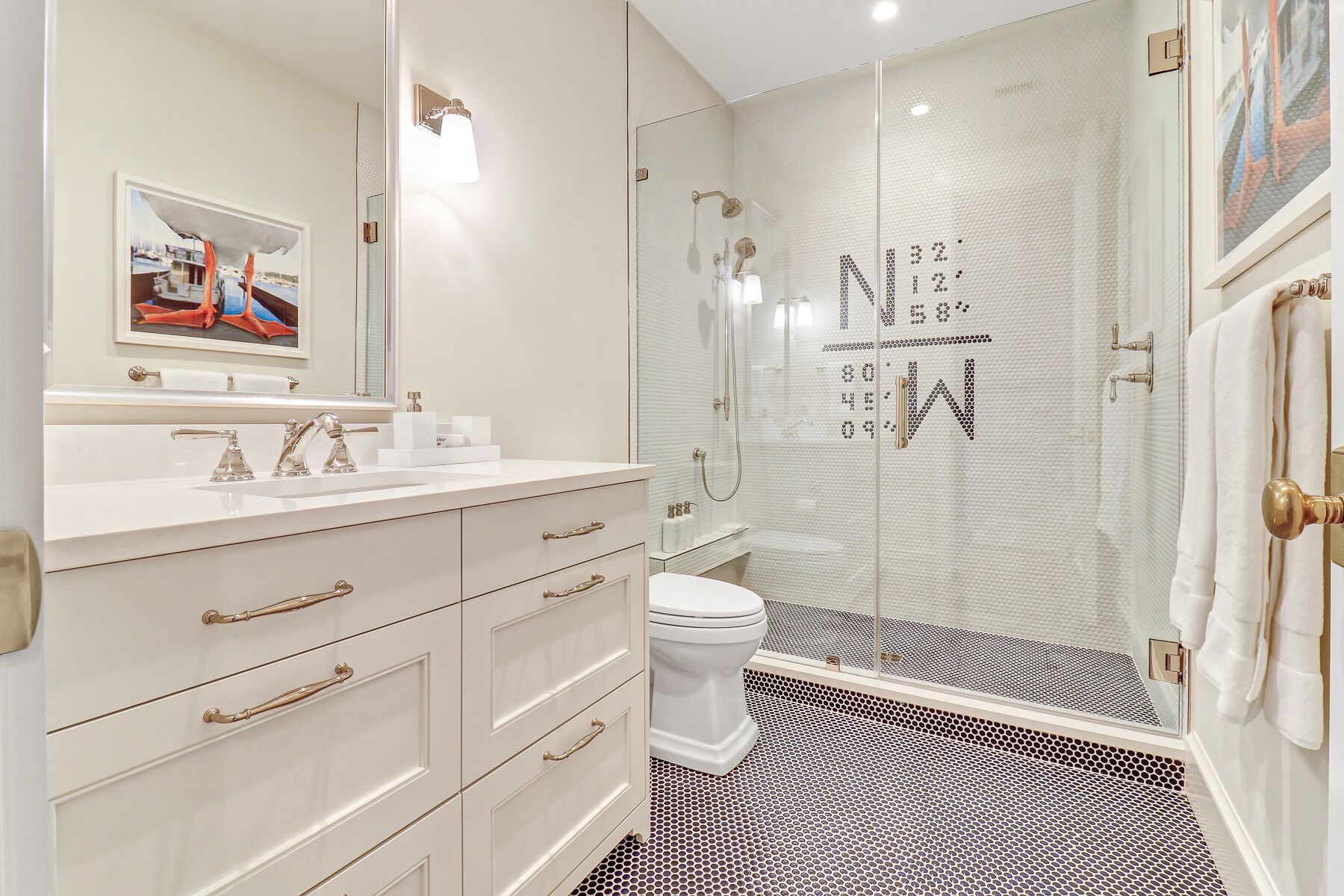 Une salle de bain moderne avec une douche à parois de verre, un lavabo blanc doté de robinetterie dorée et un grand miroir.