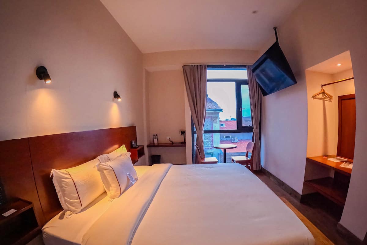 Une chambre d’hôtel avec un grand lit, une table de chevet, un téléviseur fixé au mur et une vue sur l’extérieur par une fenêtre.