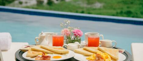 A breakfast setup with toast, eggs, and bacon on a table by a pool.