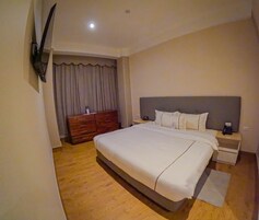 Habitación de hotel con una cama grande, piso de madera, un aparador, televisor montado en la pared y una cortina.