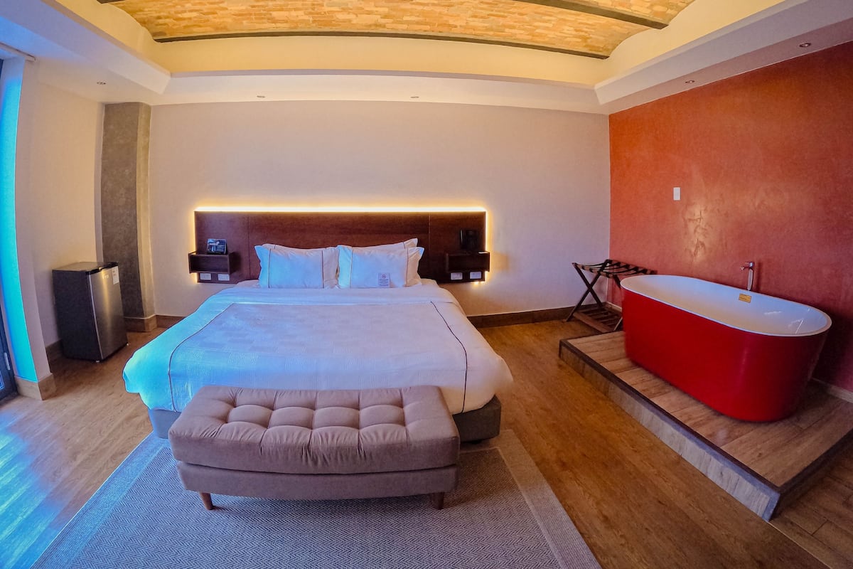 Une chambre moderne avec un grand lit, une baignoire rouge et un plafond en briques.