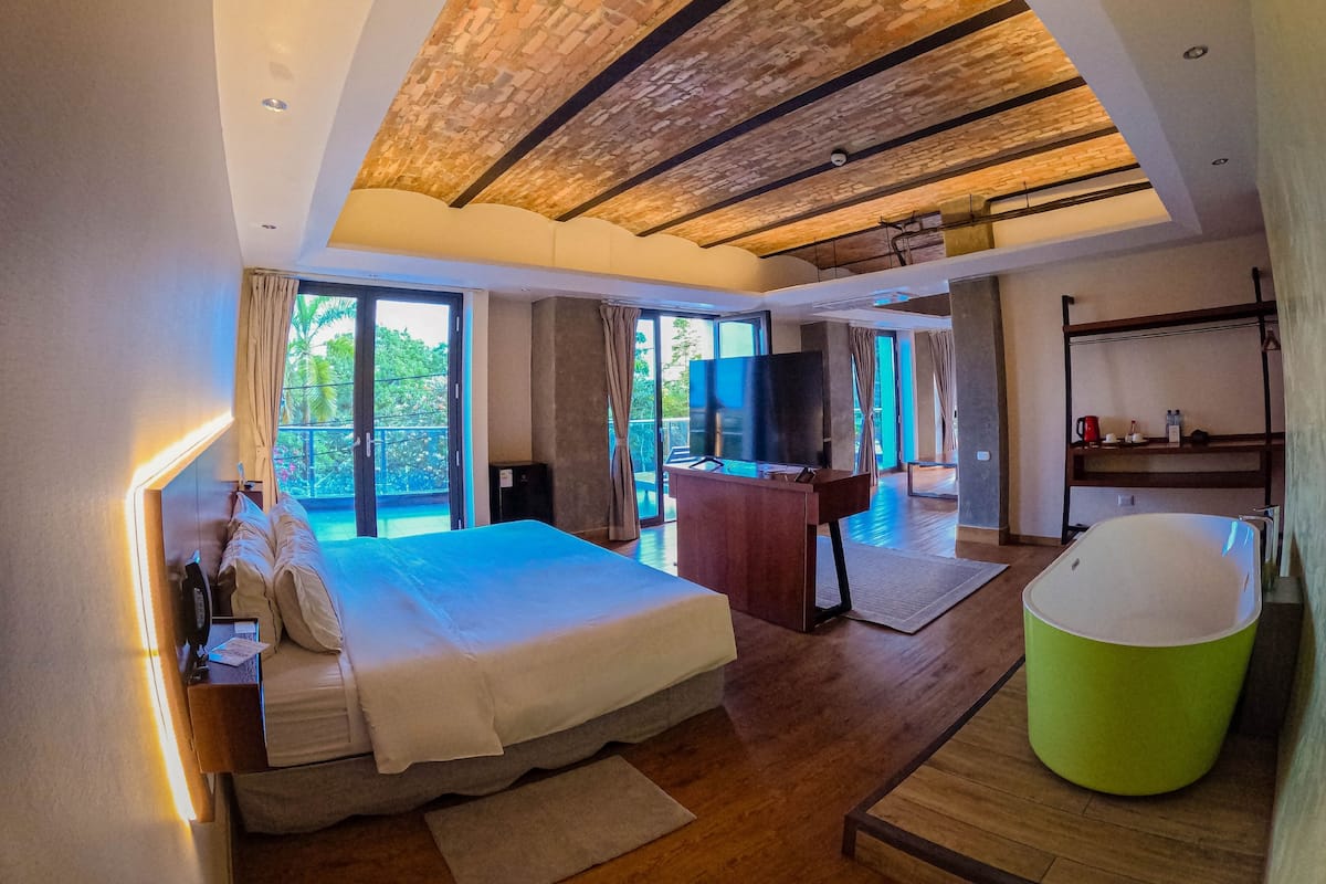 Une chambre moderne avec un grand lit, une baignoire verte et une vue sur l’extérieur.