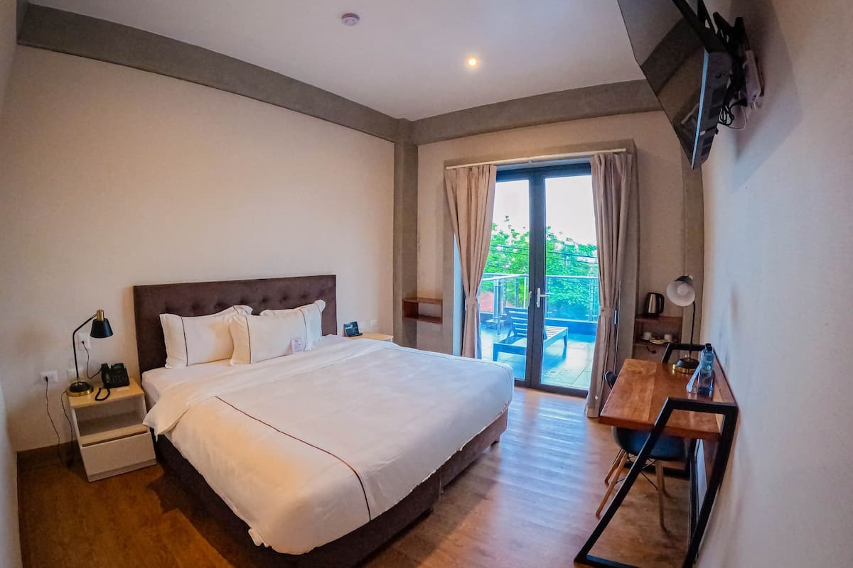 Une chambre avec un grand lit, un bureau et un balcon équipé d’une table et de chaises.