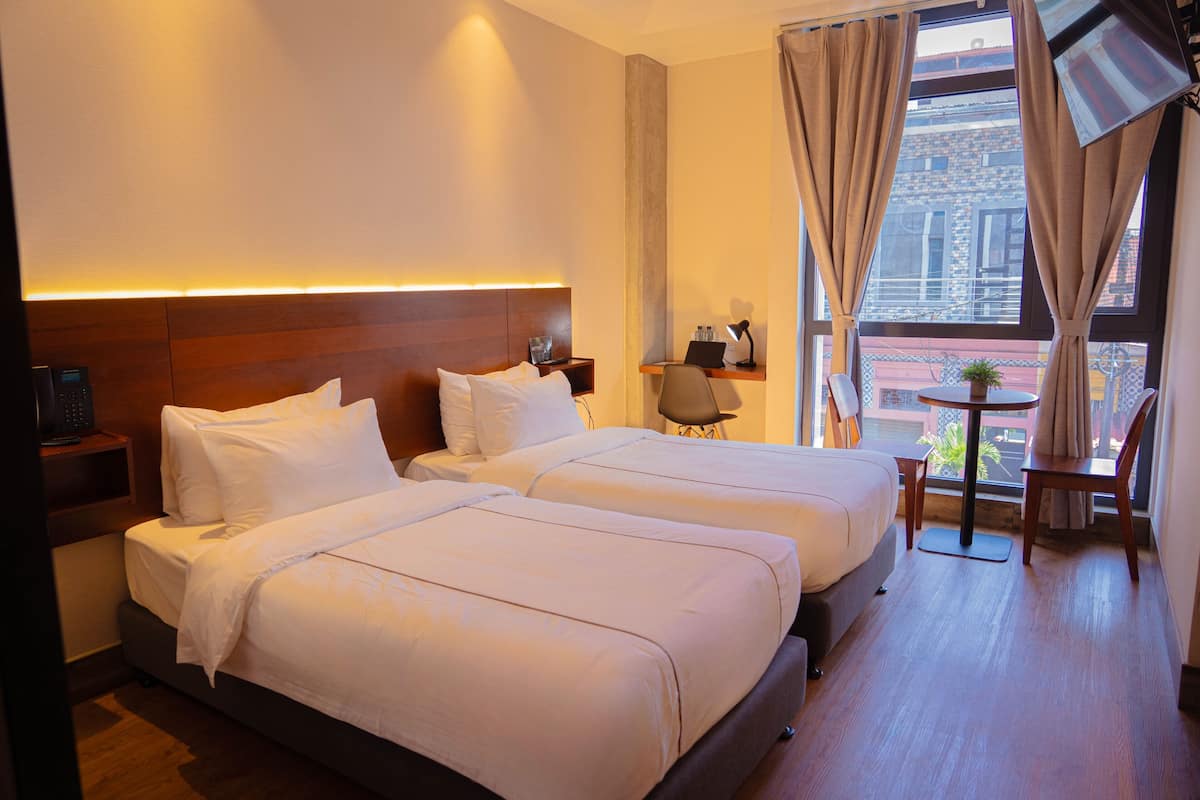 Une chambre d’hôtel avec deux lits, un bureau, une chaise et une petite table sur laquelle est posée une plante.