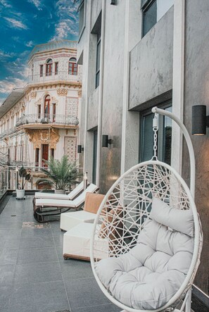 A modern building with a balcony, a hanging chair, and a small seating area with cushions.