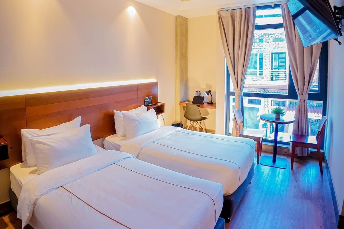 Une chambre d’hôtel avec deux lits, un bureau, une chaise, une télévision et une grande fenêtre avec des rideaux.