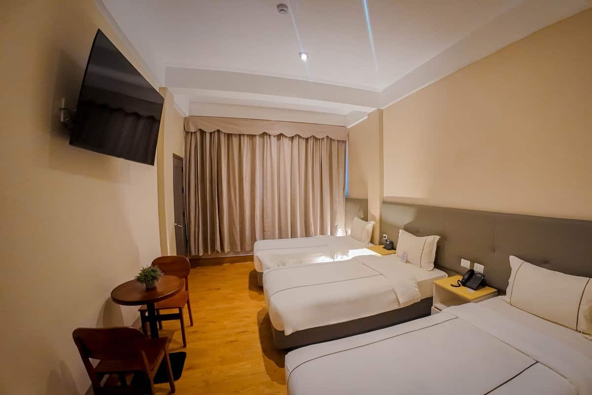 Une chambre d’hôtel avec deux lits, un bureau avec une chaise, un téléviseur fixé au mur et une fenêtre avec des rideaux.