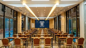 A conference room with rows of tables and chairs, large windows, and a banner with a logo.