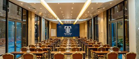 A conference room with rows of tables and chairs, large windows, and a banner with a logo.