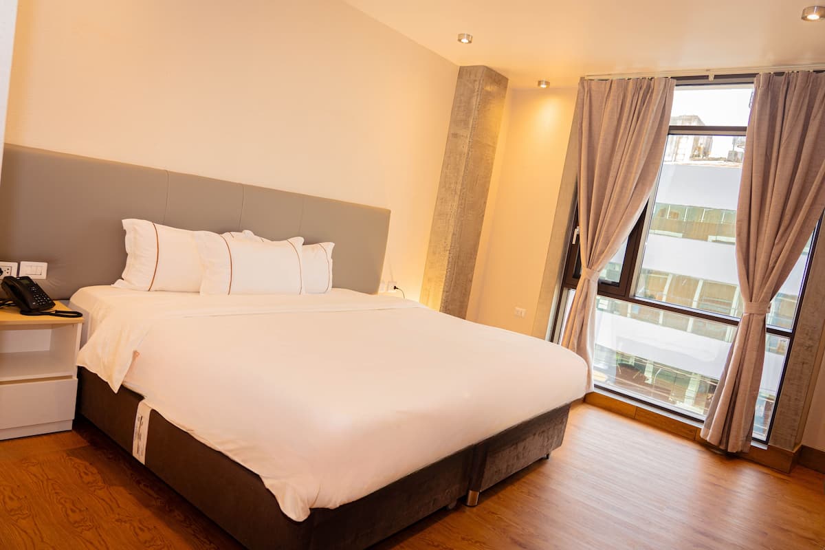 Une chambre d’hôtel avec un grand lit, un téléphone sur la table de chevet et une fenêtre avec des rideaux.