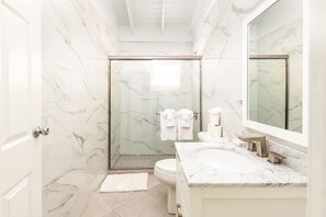 Un baño moderno con ducha de mampara de vidrio, inodoro blanco y encimera de mármol.