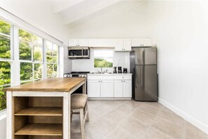 Une cuisine moderne avec des meubles blancs, des appareils en acier inoxydable, une table en bois et une fenêtre donnant sur un espace verdoyant.