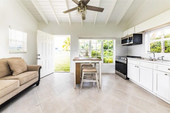 Una cocina con armarios blancos, encimera de madera, ventilador de techo y vistas al exterior.