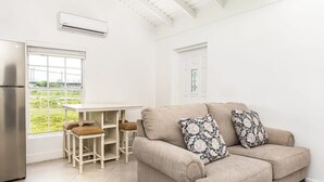 Een moderne keuken met een inbouwfornuis, een eethoek met een tafel en stoelen, en een beige bank met gekleurde kussens.