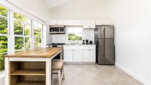 Een moderne keuken met witte kasten, roestvrijstalen apparatuur, een houten tafel en een raam met uitzicht op groen.