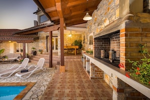 Un edificio de piedra con piscina, sillas de descanso y zona de barbacoa.